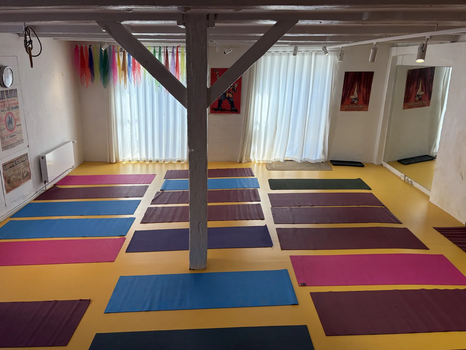 Salen med yogamåtter på det gule gulv, lyse gardiner og røde malerier på væggen
