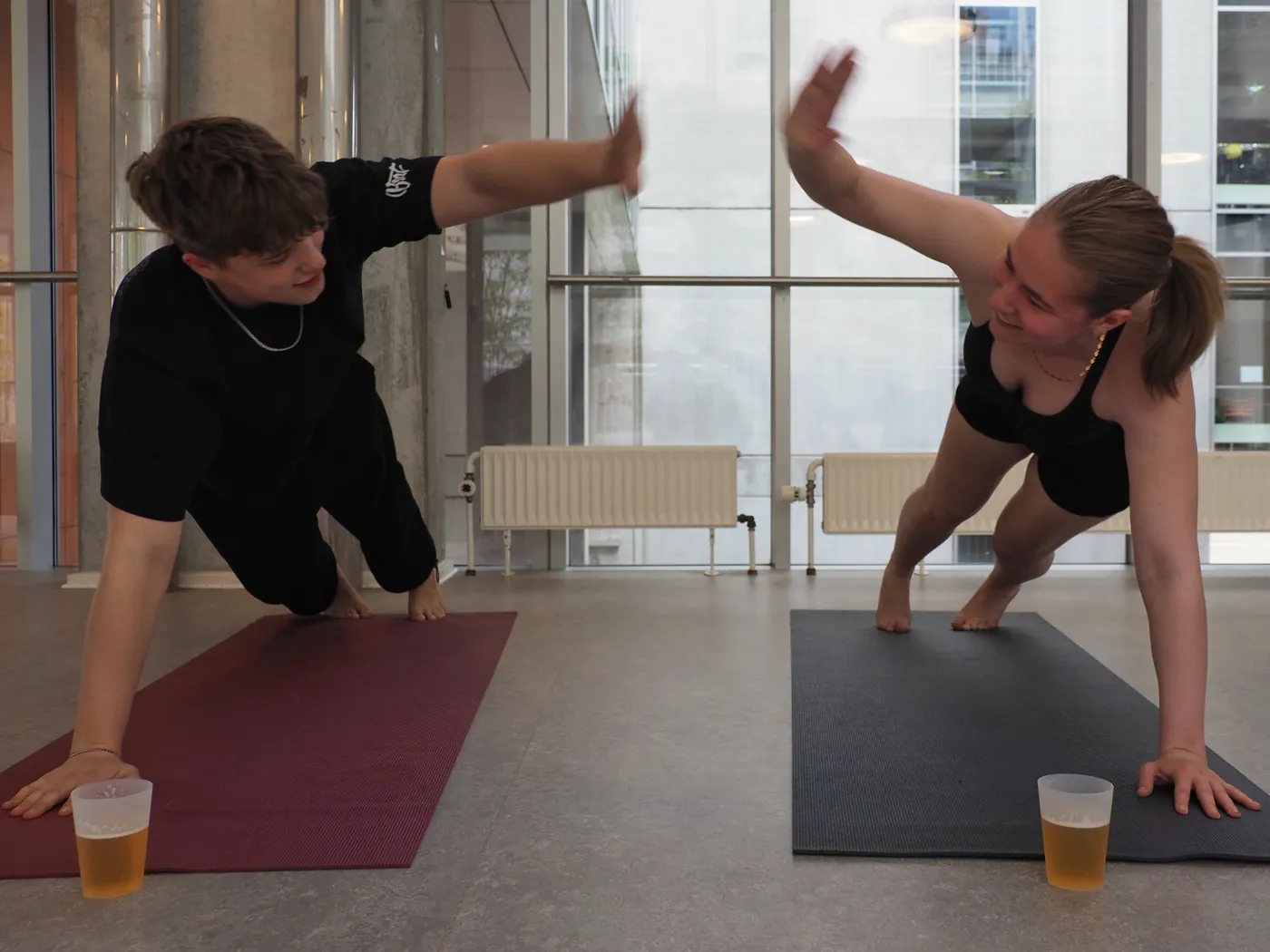 To deltagere giver high five i sideplanke med ølglas på måtterne
