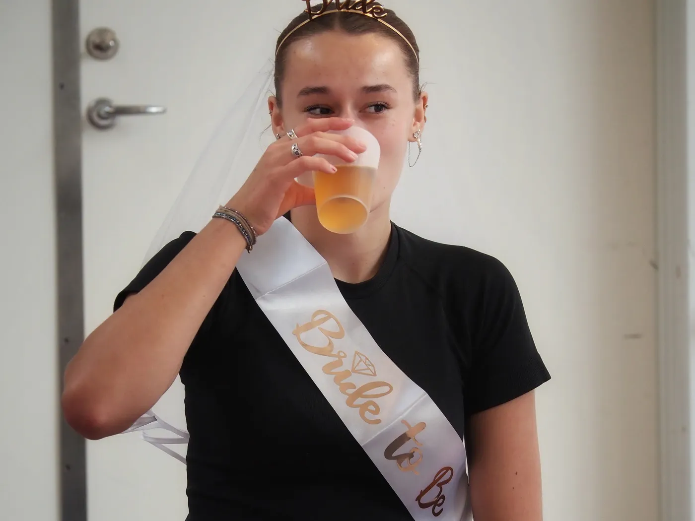 Bruden med slør og «bride to be»-skærf drikker af sit glas
